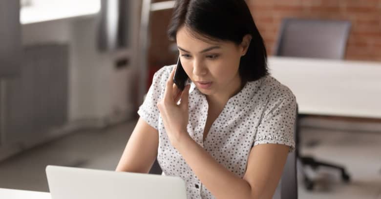 A woman sits in front of a computer talking on the phone with a customer service representative.