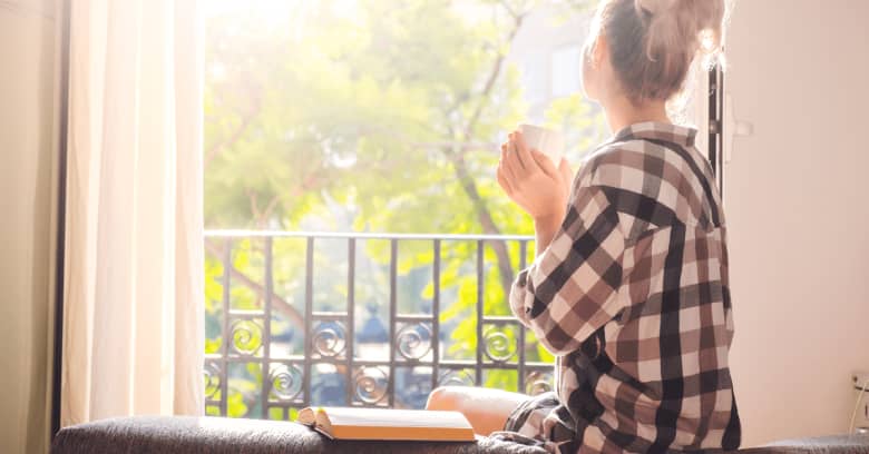 A woman looks out the window while drinking a cup of coffee.
