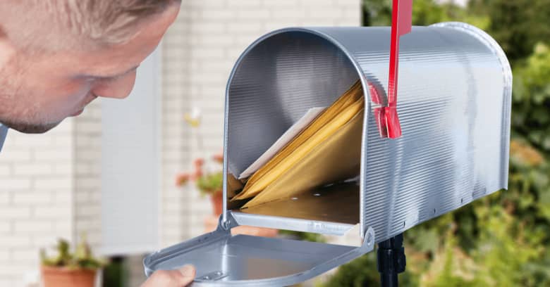 A man is peering into a silver mailbox to see if his stimulus check has arrived
