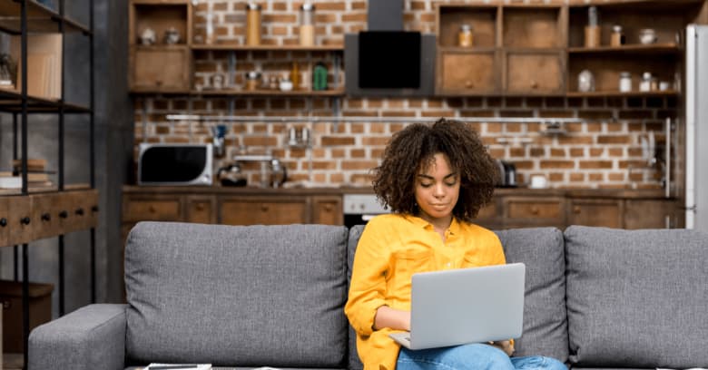 A woman sits on the couch of her home with her computer