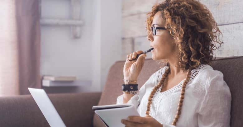 a woman takes notes while looking off into the distance with a computer in her lap