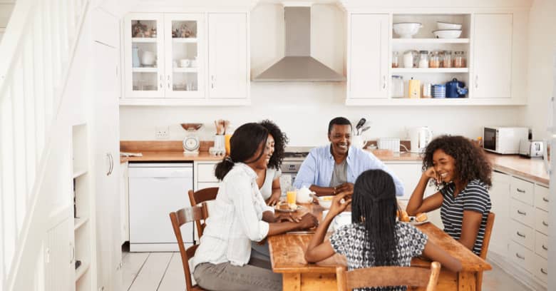 a family consisting of parents and teenage children has a meal together at a table in the kitchen