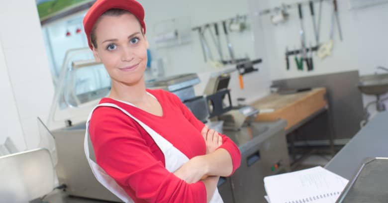 A food service worker is seen in an industrial kitchen with a smile on her face