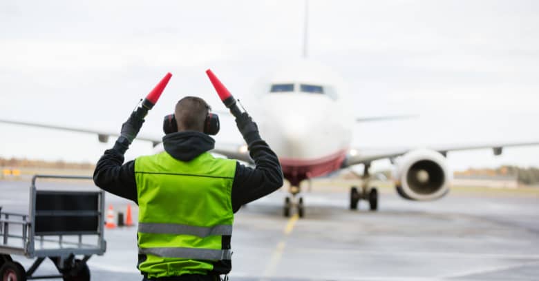 A member of a flight ground crew directs a commercial airplane into a terminal