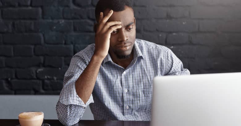 a man looks at his computer with worried facial expression and hand gestures