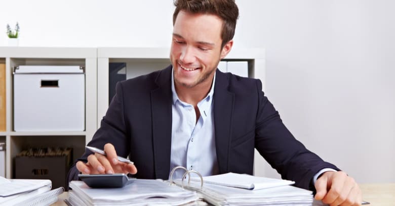 a man is smiling while pressing the buttons of his calculator and taking notes