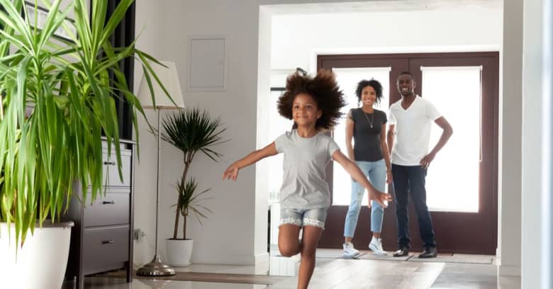 a little girl running around the house while her parents are looking at her smiling