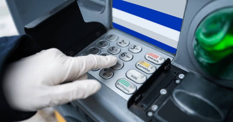 A gloved hand is seeing operating a bank ATM