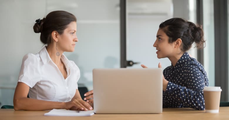 2 Women sit at a laptop computer and have a serious discussion about salary