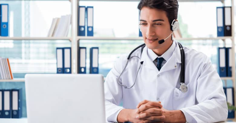 a doctor is seen at a desk conducting a telehealth appointment with his patient.