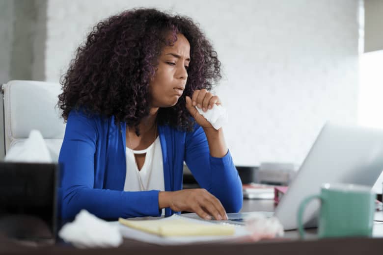 a woman is coughing into a tissue while looking at her computer