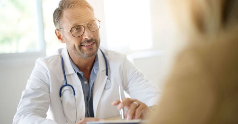 A doctor holds a clipboard while talking to a patient