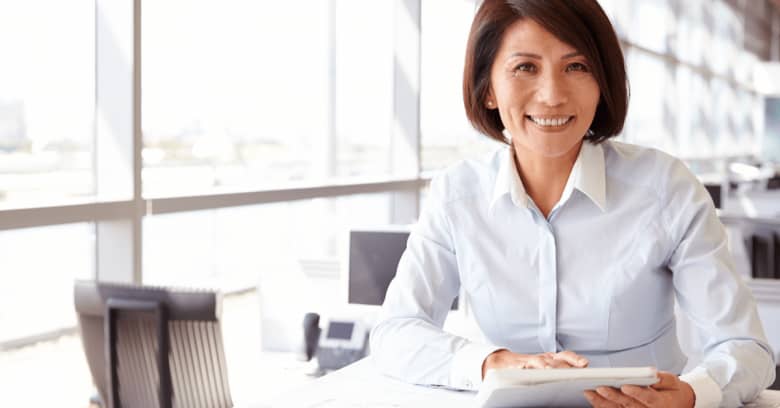 a woman sits at a desk looking at papers with a happy expression