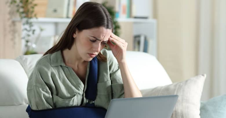 A worried woman with an arm sling reads a letter about her denied health insurance claim.