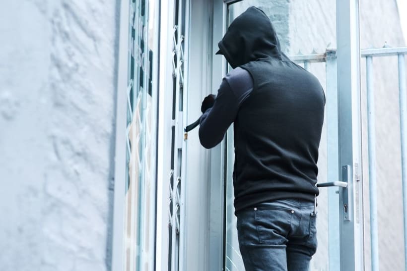 A burglar uses a crowbar to open a front door.