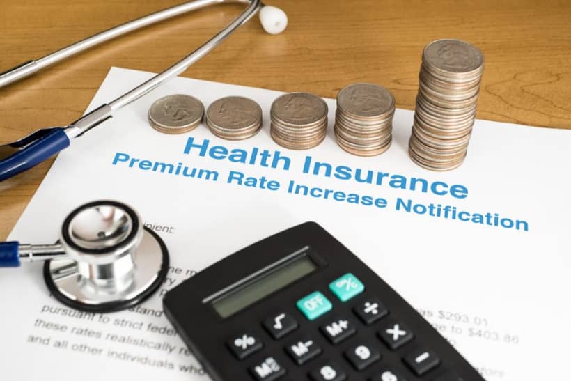 Notice of health insurance premium increase with stacked coins, stethoscope and calculator on overlayed