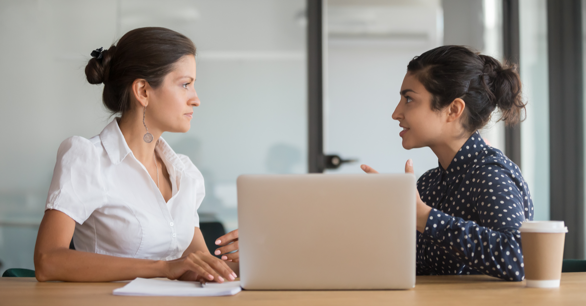 2 Women sit at a laptop computer and have a serious discussion about salary