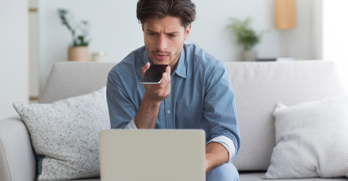 a man sits in front of his computer speaking into his phone while looking concerned