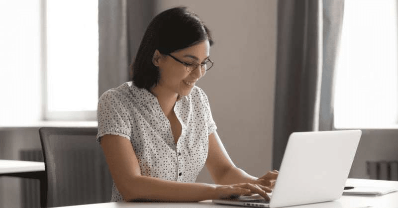 A woman looks at her computer with a smile on her face. She is relieved to have settled medical debt.