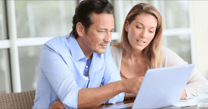 A couple sits together at a table looking at their computer and discussing medical bills.