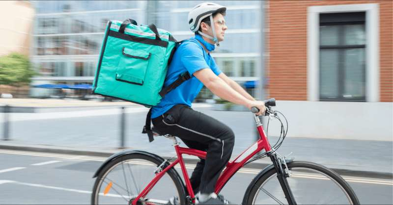 A gig worker rides a bike with a grocery delivery.