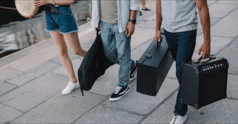 A group of freelance musicians are seen walking on a city street sidewalk while carrying their instruments to their gig.