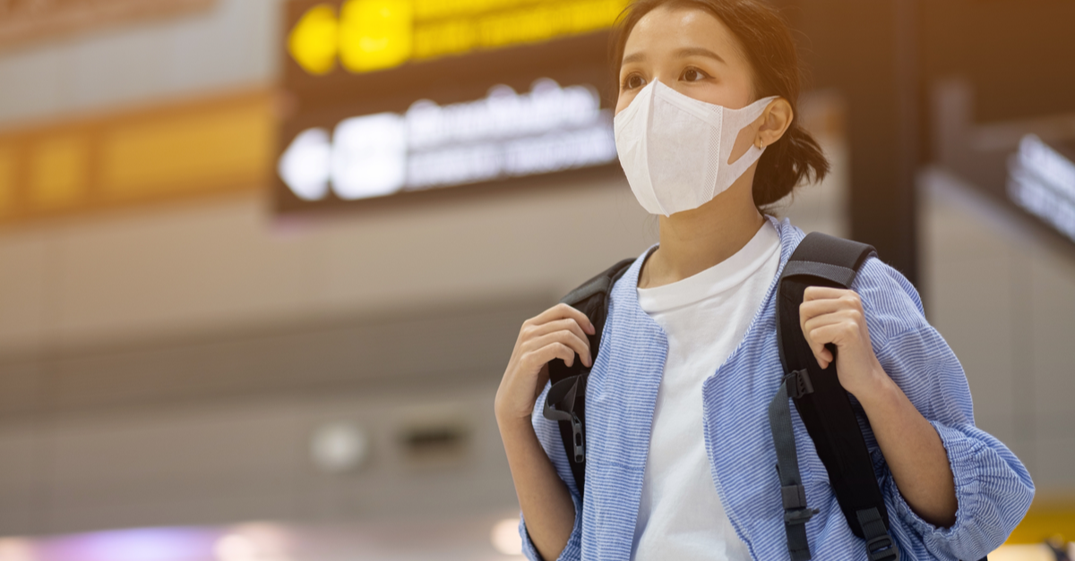 A young woman wearing a mask carries her backpack through the airport.