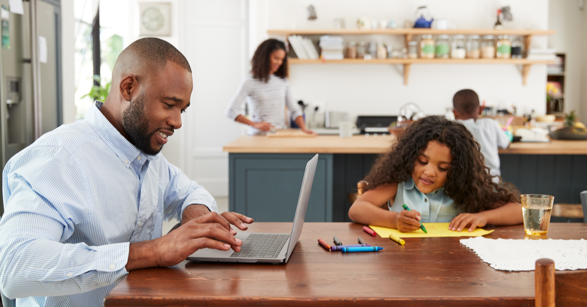 A man looks at life insurance options on his computer while his family engages in various activities nearby