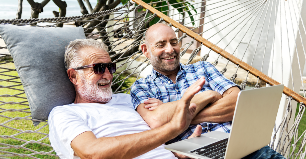 2 men enjoy looking at a computer while they sit in a hammock