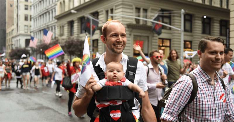 Two dads enjoy a pride parade with their baby