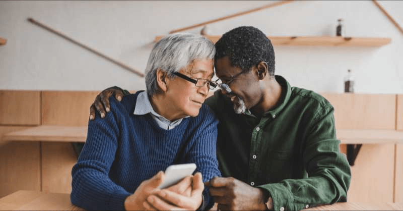 Two senior LGBT men enjoy a moment together looking at their phone and smiling