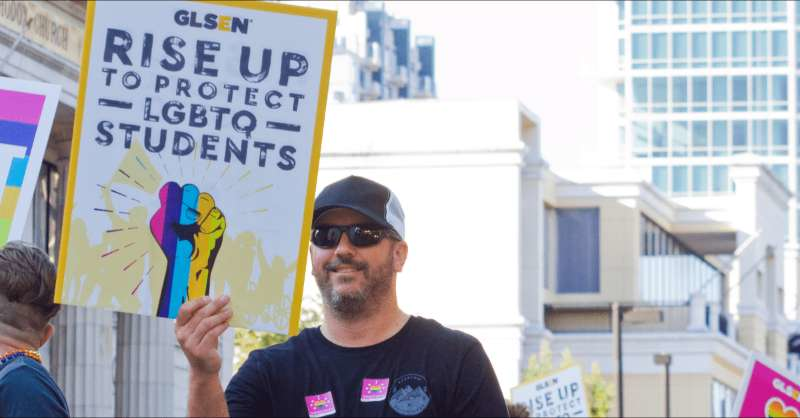 a participant of a pride parade displays a GLSEN sign in support of LGBTQ+ K-12 students