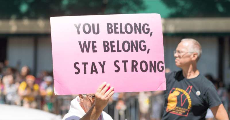 A man holds a sign that reads, 'You Belong, We Belong, Stay Strong.'