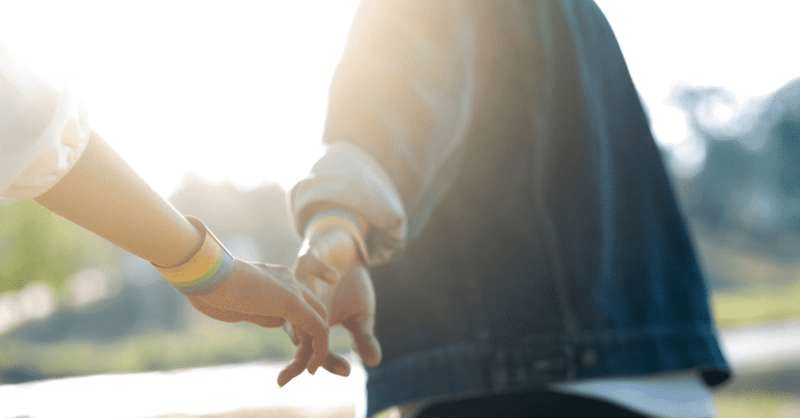 two people with rainbow bracelets hold hands