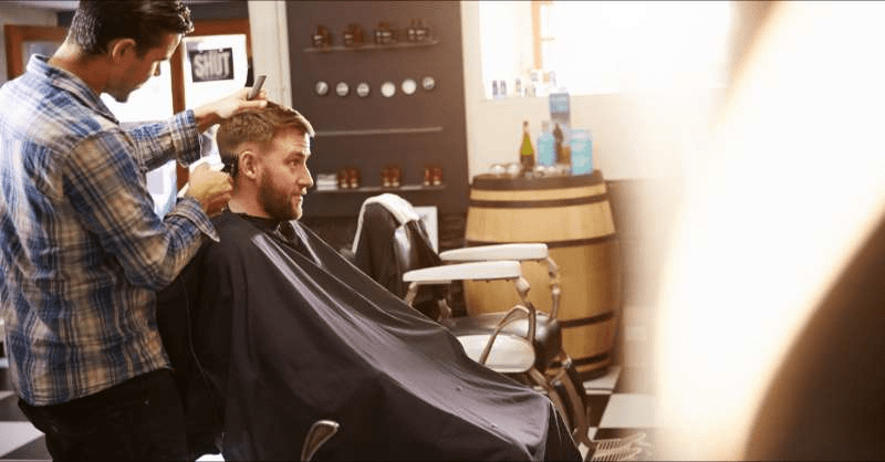 A barber who owns his own shop cuts a client's hair