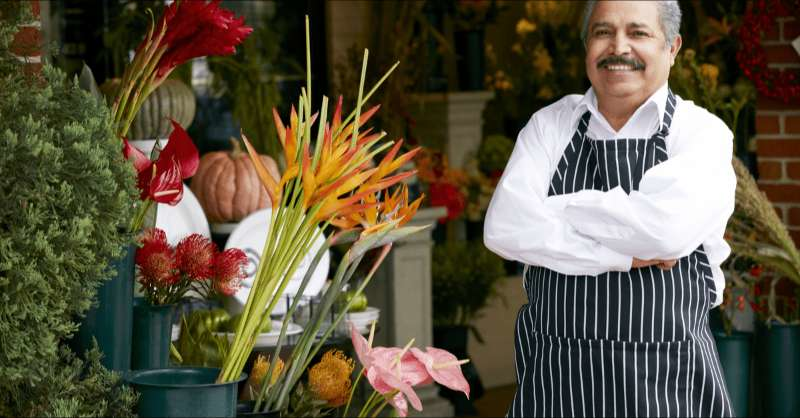 A man who owns his own floral shop poses in front of a display of flowers