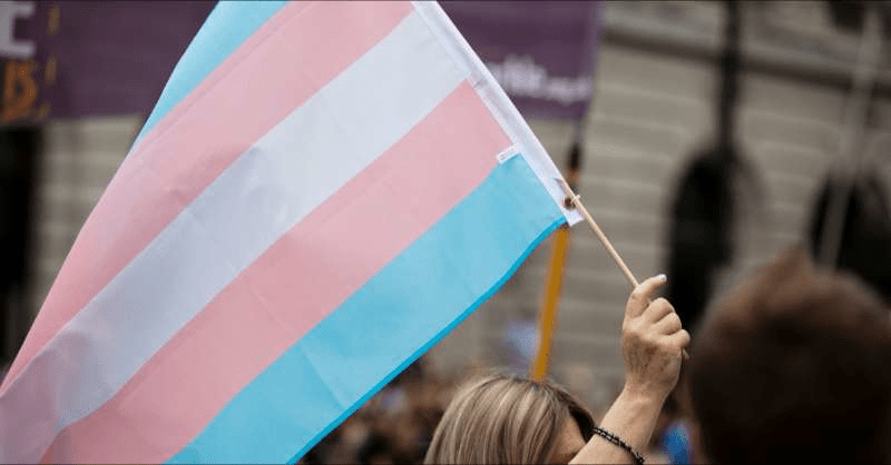 A woman holds a trans pride flag in the colors of pink, blue and white