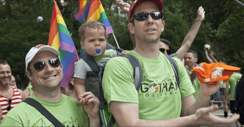 two dads appear at a Pride Month celebration with their toddler child