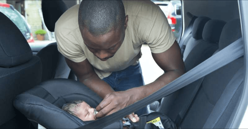 an LGBTQ+ dad gets his newborn son settled in a car seat.