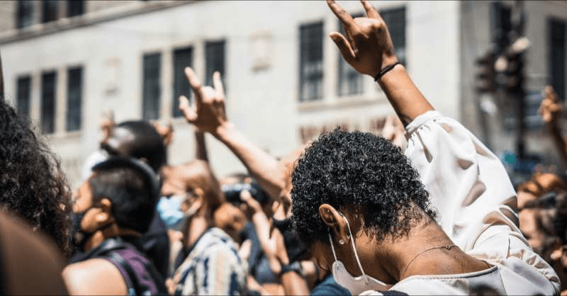 A crowd of protesters is shown with heads bowed and giving the sign language sign for 'love'