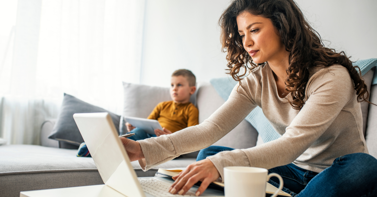 A woman works from home while her son sits in the background