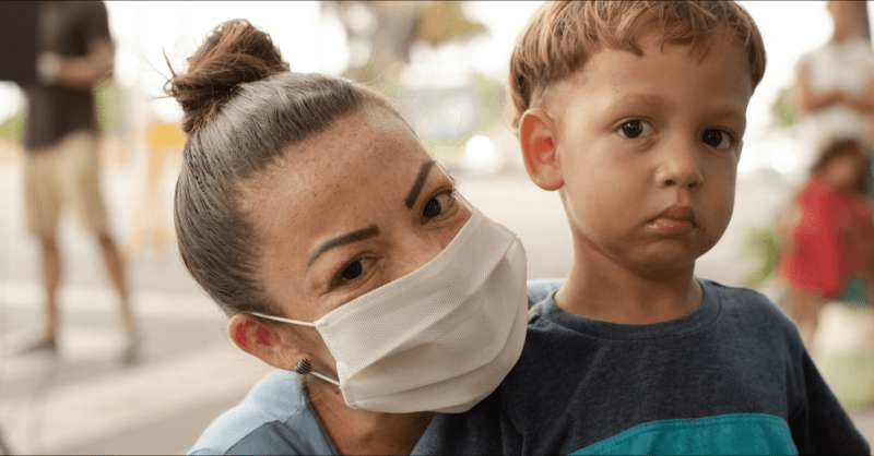 A woman wearing a mask embraces a little boy being helped by a charity during COVID-19.