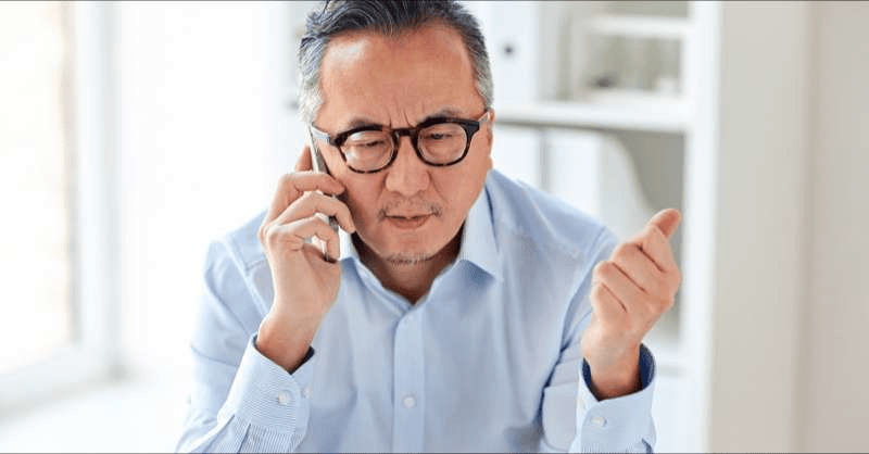 A man is called on the phone regarding giving a donation and shows a skeptical look on his face as the caller asks for personal information.