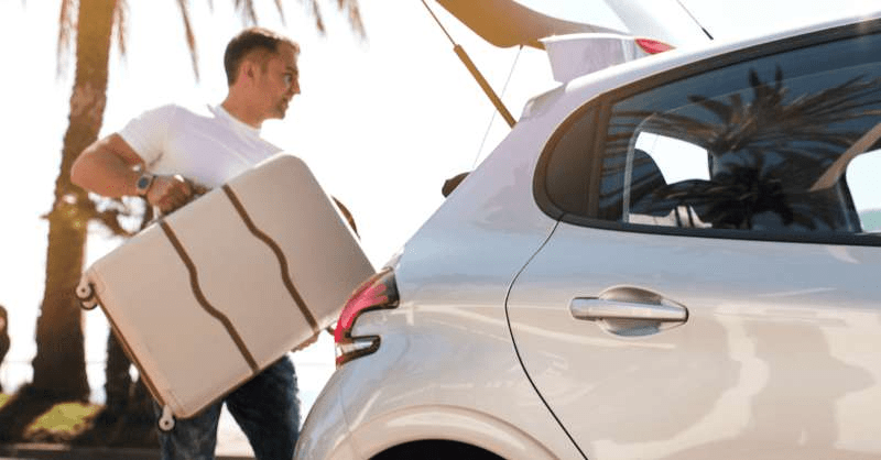 A man loads a suitcase into a rented vehicle