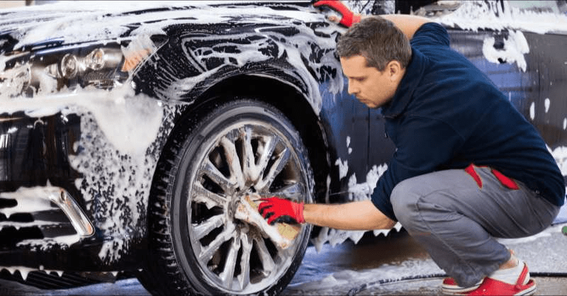 A car wash employee scrubs the tires of a car