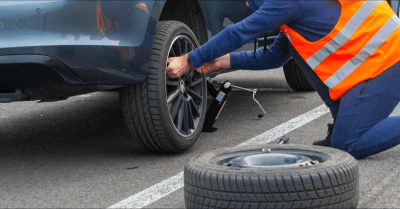 A roadside assistance service worker changes a tire at the side of the road