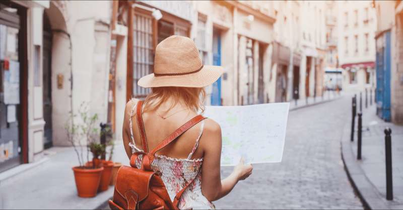 A woman walks on a small road in a European town as she holds a map