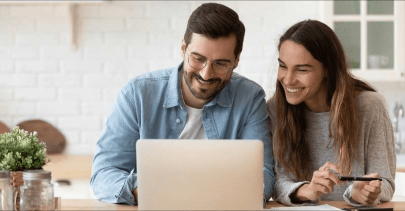 A couple sits at a table with a laptop computer in front of them.