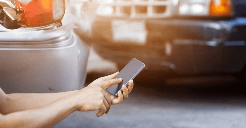 A person uses their cell phone after a car accident to document the damage