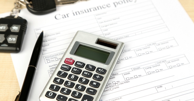 A car insurance policy is laid out on a table with a set of car keys in the left-hand corner, a black pen pointing up is right next to a calculator that is front and center.